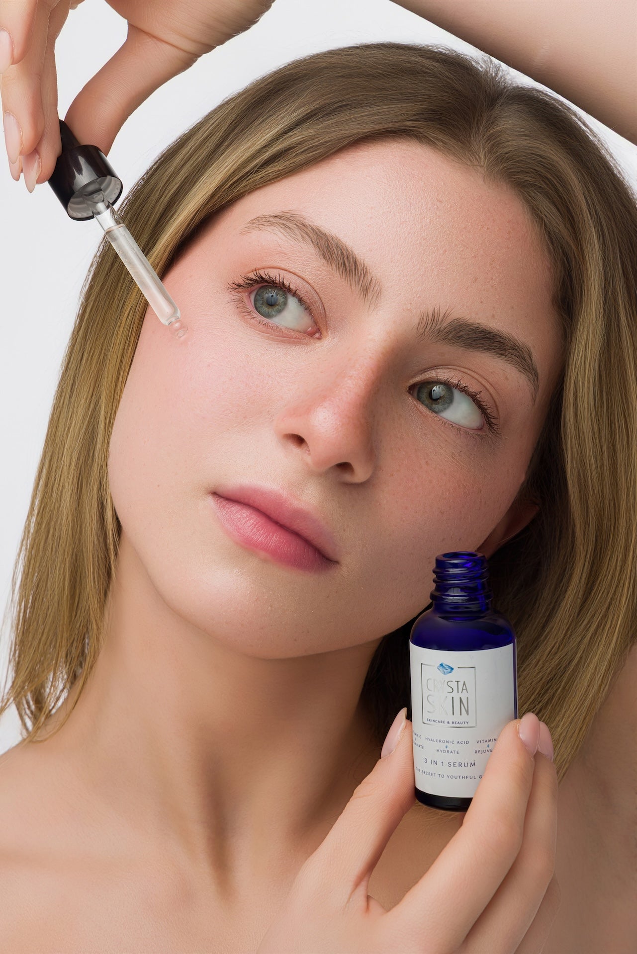 Woman applying skincare product with dropper and bottle on a white background