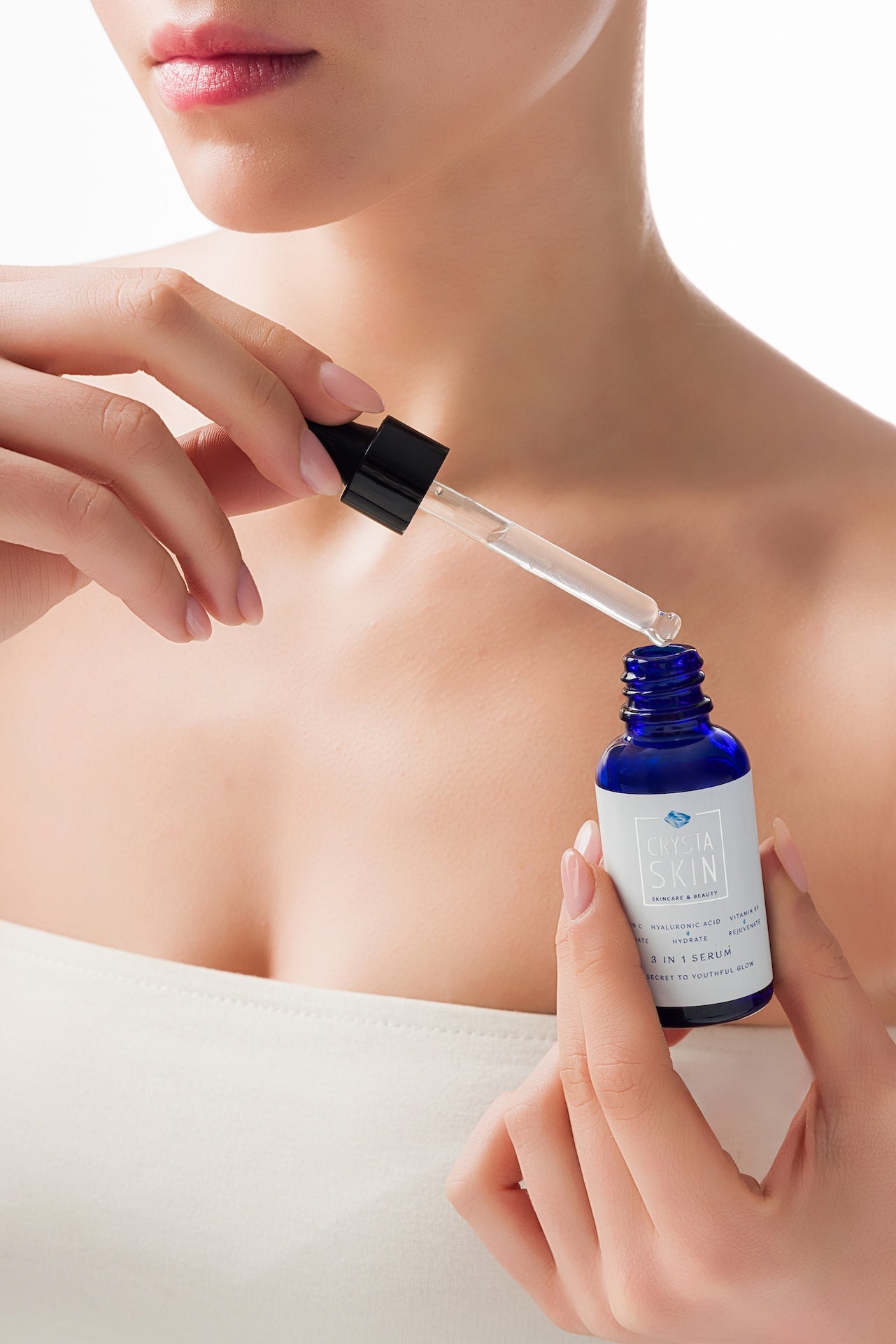 Person applying a dropper of serum to their skin with a blue dropper bottle.